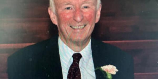 Image of Richard Walters provided by family. He is wearing a black suit jacket with a white buttoned shirt, a rose in his lapel pocket. He has grey hair and is smiling.