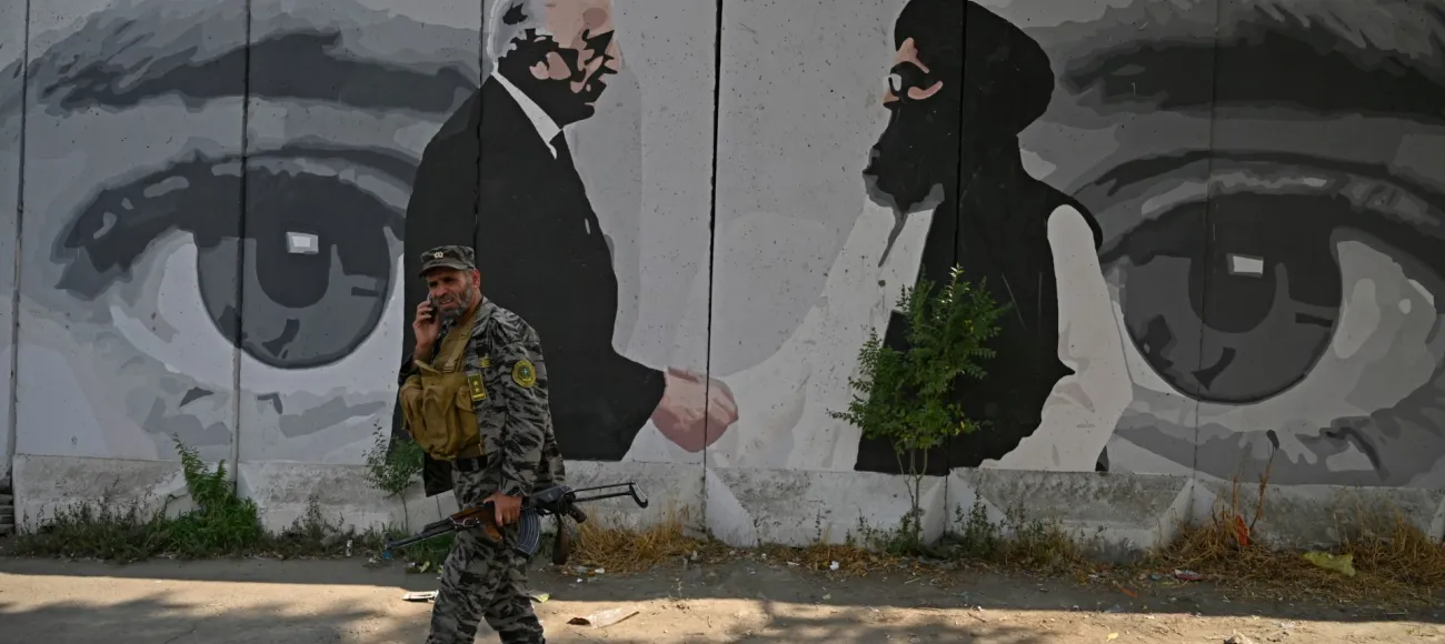 "A security personnel walks past a wall mural with images of US Special Representative for Afghanistan Reconciliation Zalmay Khalilzad (L) and Taliban co-founder Mullah Abdul Ghani Baradar, in Kabul on July 31, 2020 / Wakil Kohsar / AFP via Getty Images"
