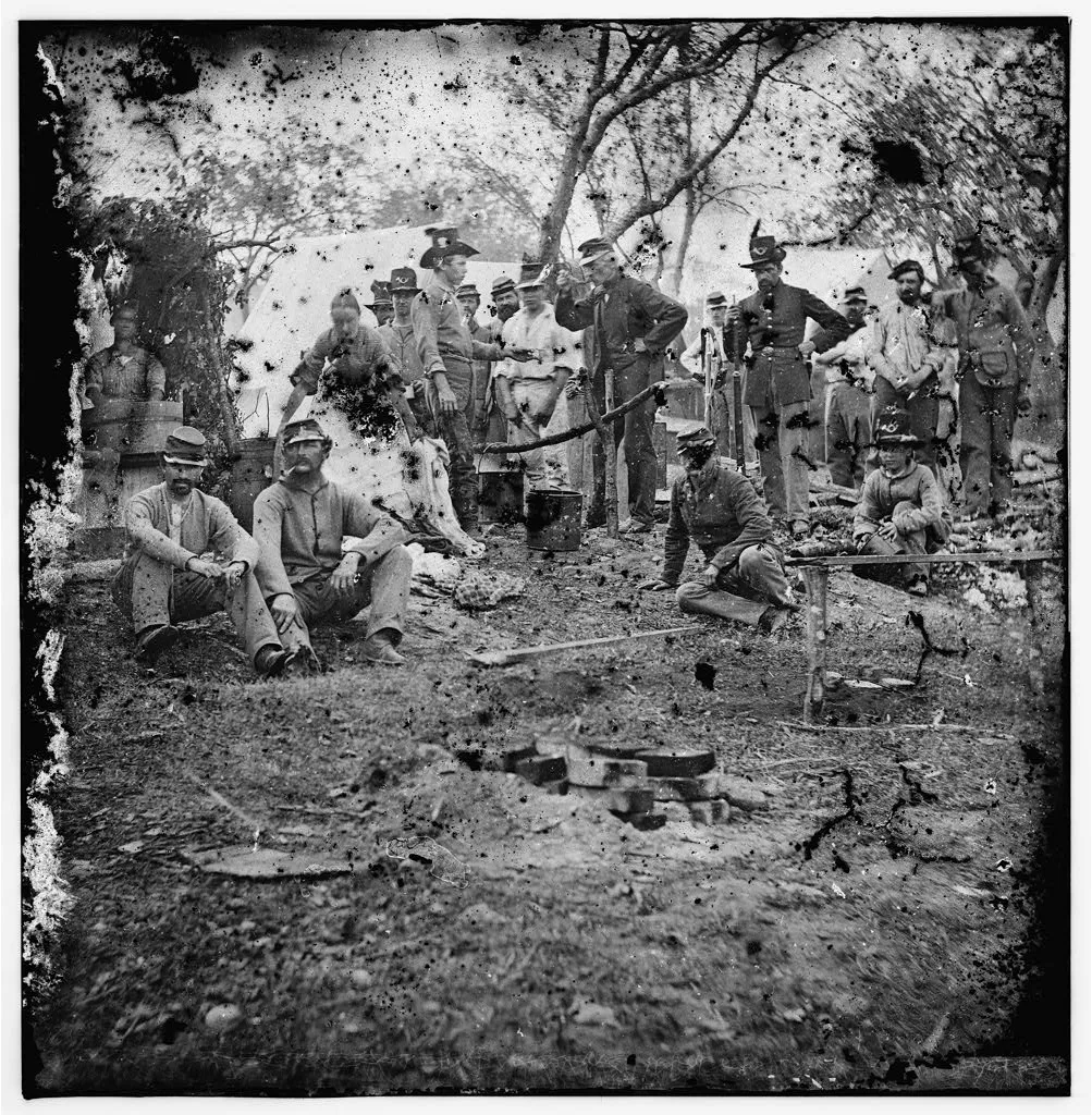 "Black and white photo from the civil war, cooking around a fire"